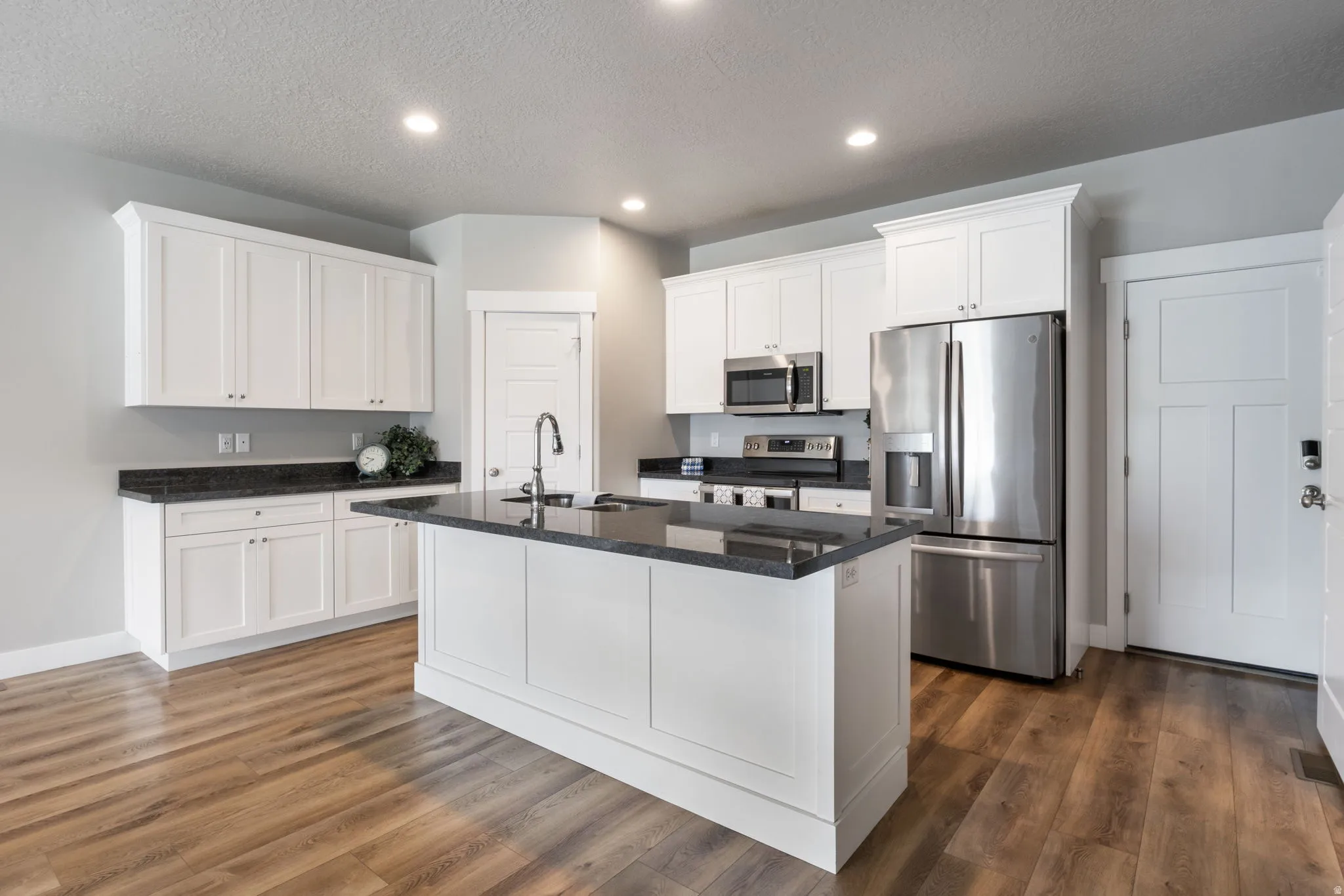 Modern kitchen featuring a central island, white shaker cabinetry, dark countertops, stainless steel appliances, and wood-finish flooring