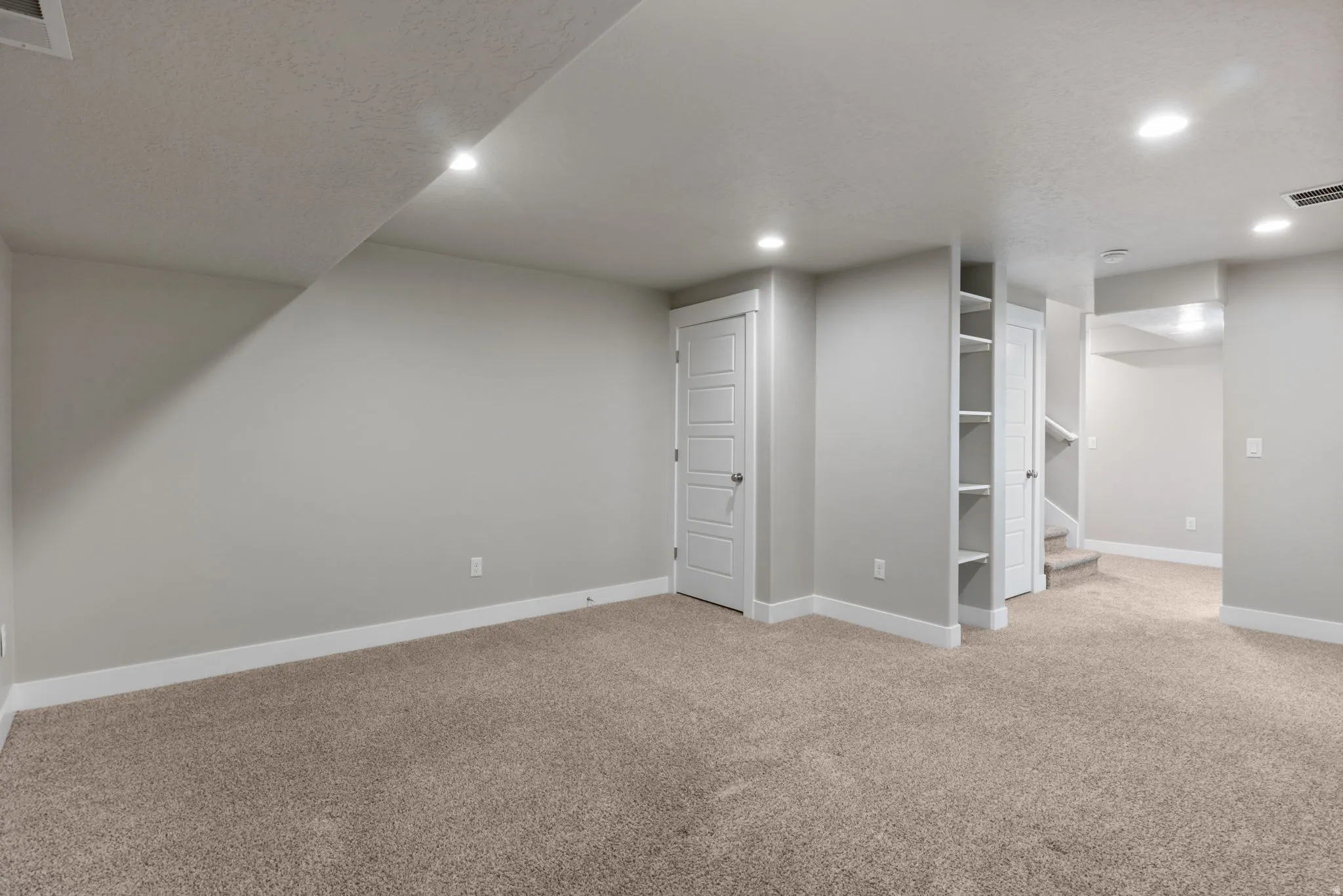 Spacious interior room featuring light gray walls, neutral carpet, recessed lighting, and white trim