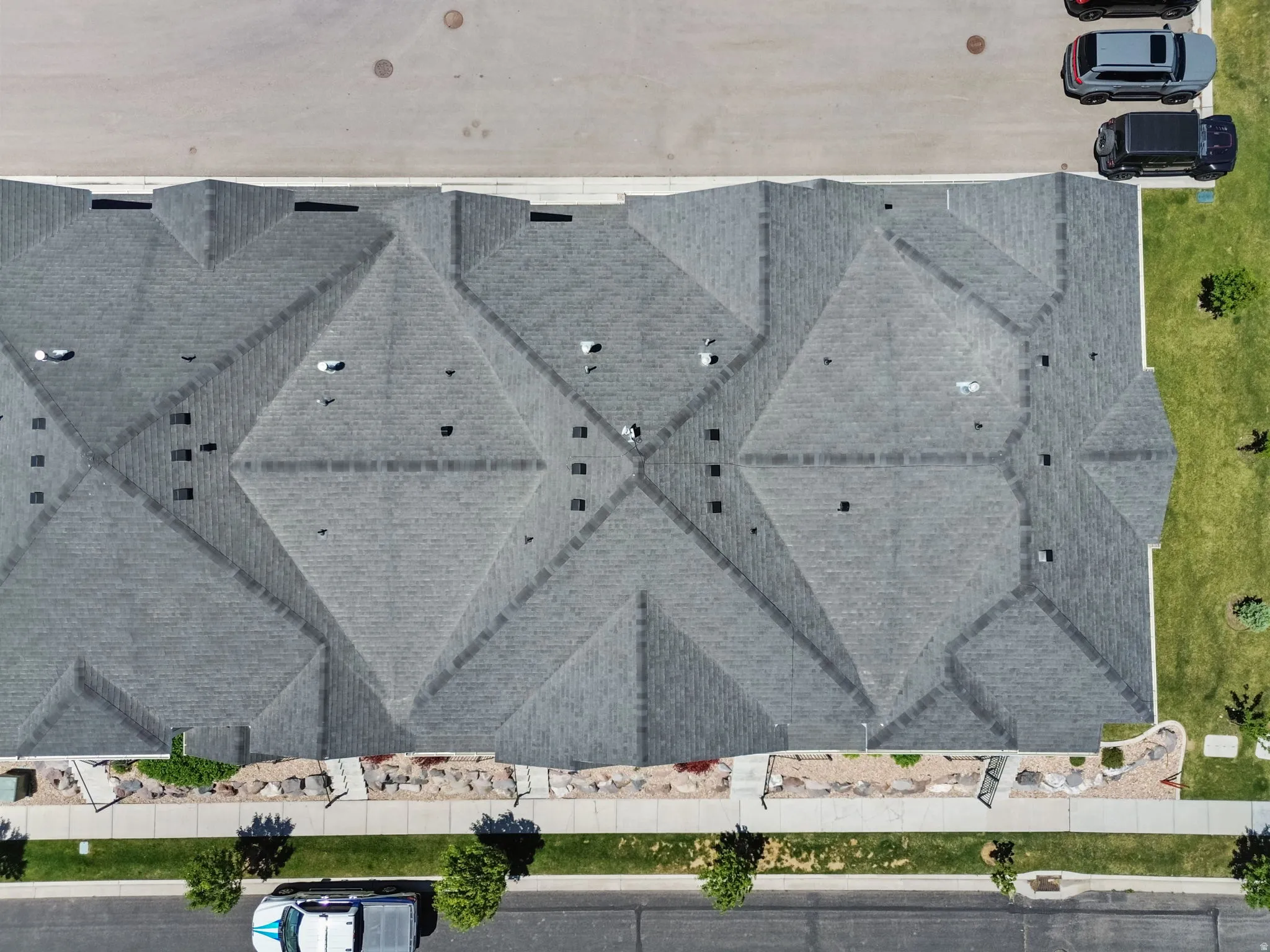 Multi-unit residential structure featuring a complex shingle roof system, multiple roof vents, and a paved parking area