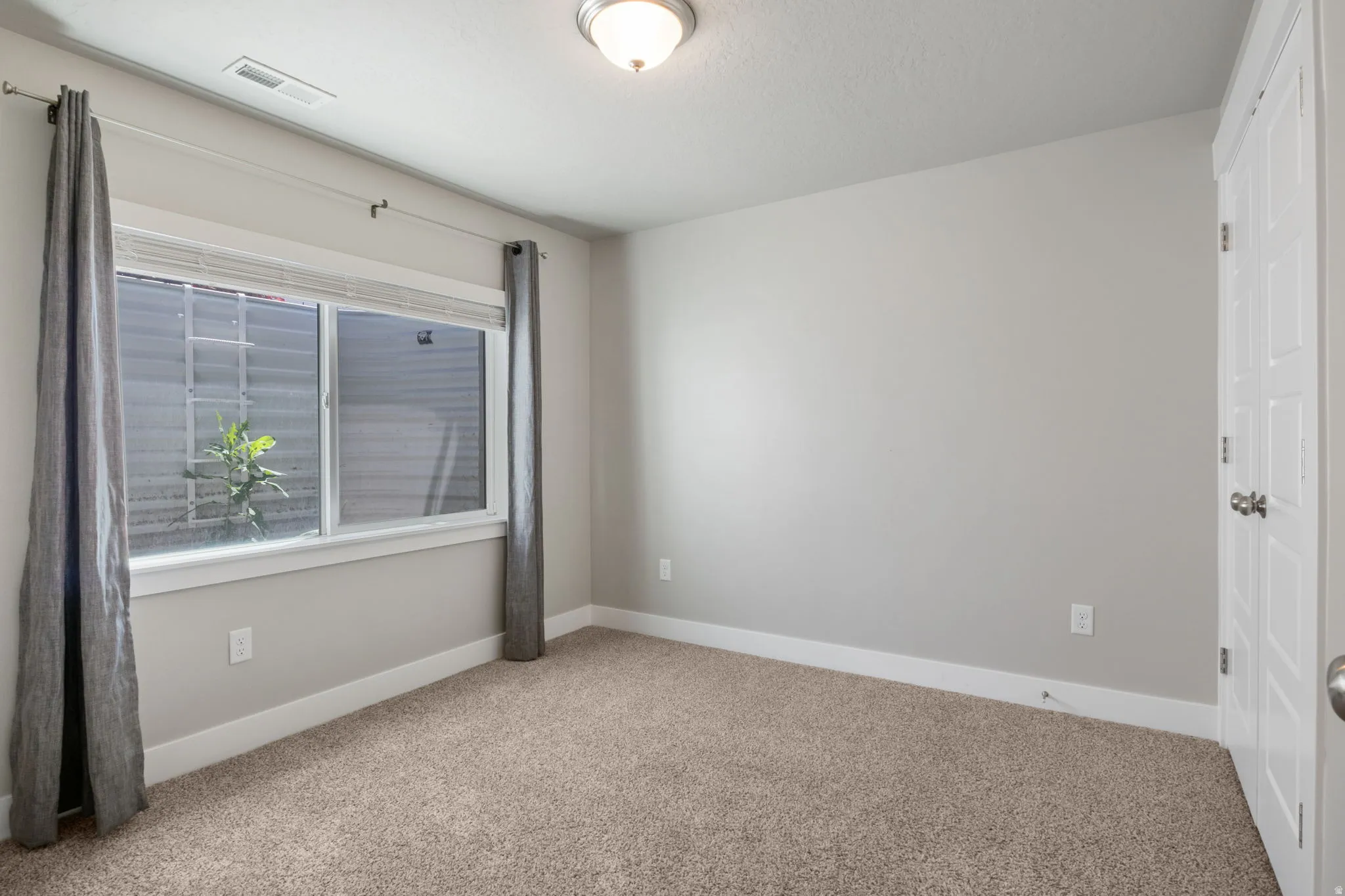 Carpeted room featuring a double window with a white frame and blinds, light gray wall paint, white baseboards, and a white paneled door