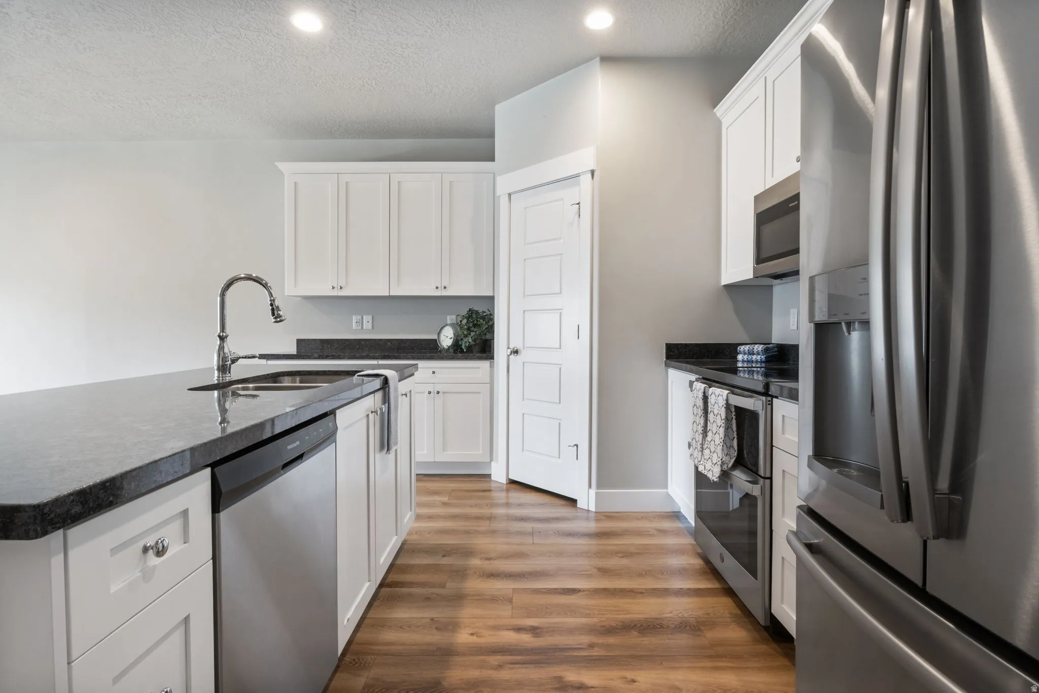 Modern kitchen featuring white cabinetry, dark countertops, stainless steel appliances, wood-finish flooring, and recessed lighting