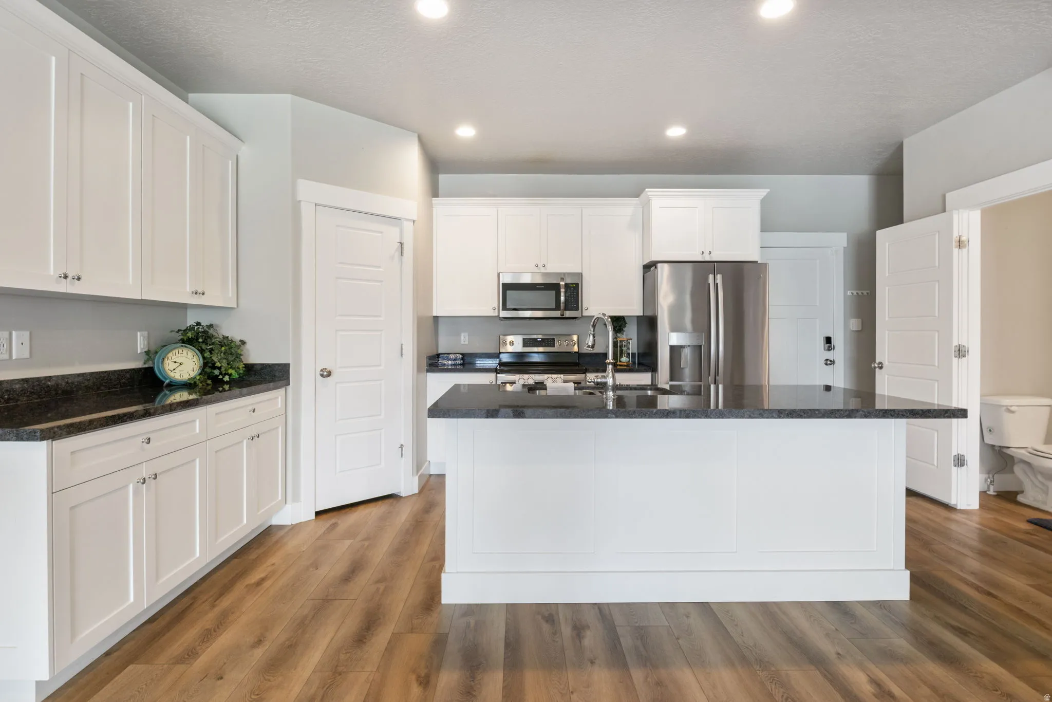 Kitchen featuring white cabinetry, dark stone countertops, stainless steel appliances, and wood-finish flooring