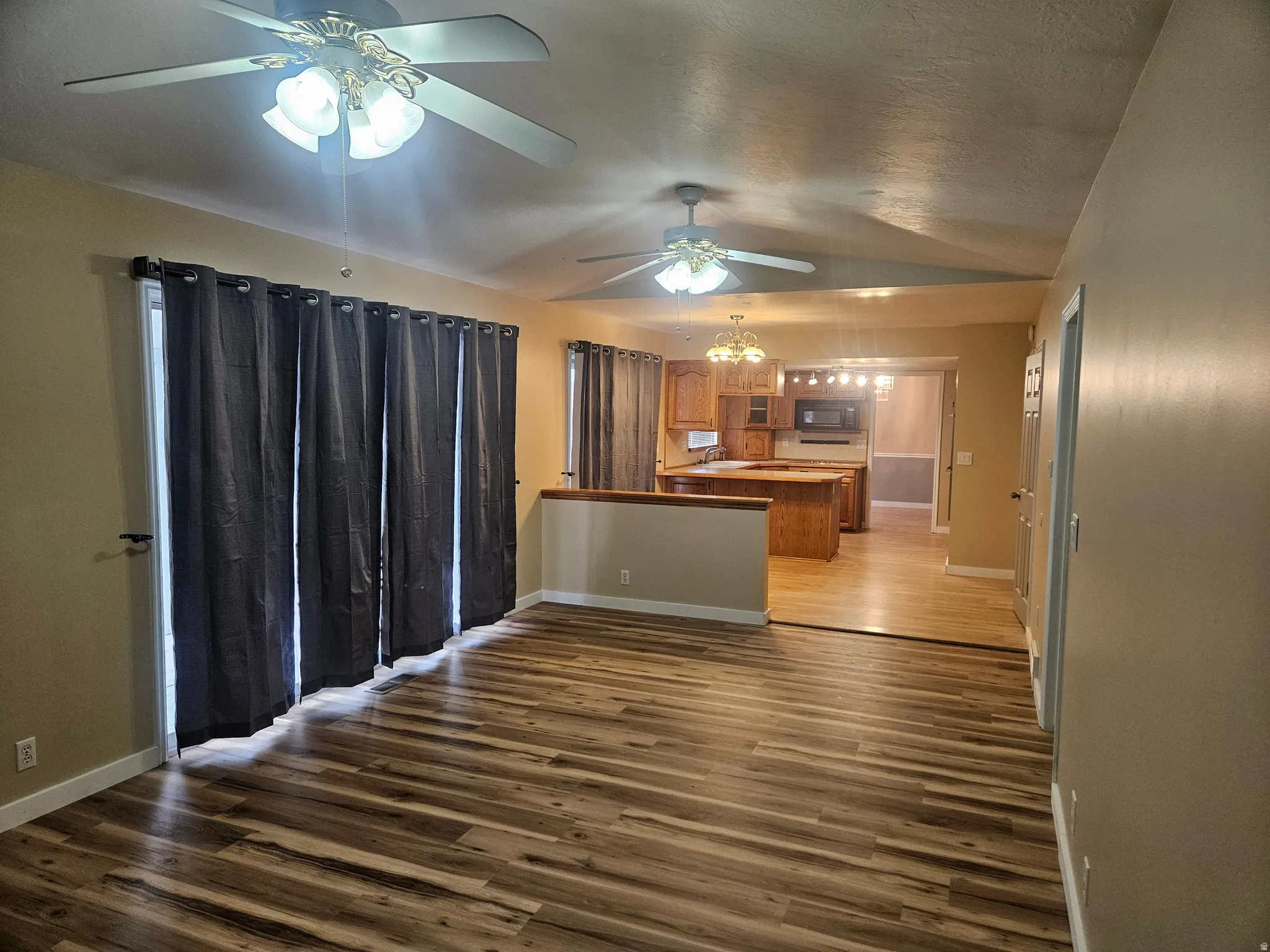 Open-concept living area featuring wood-finish flooring, ceiling fans with integrated lighting, and a sliding glass door