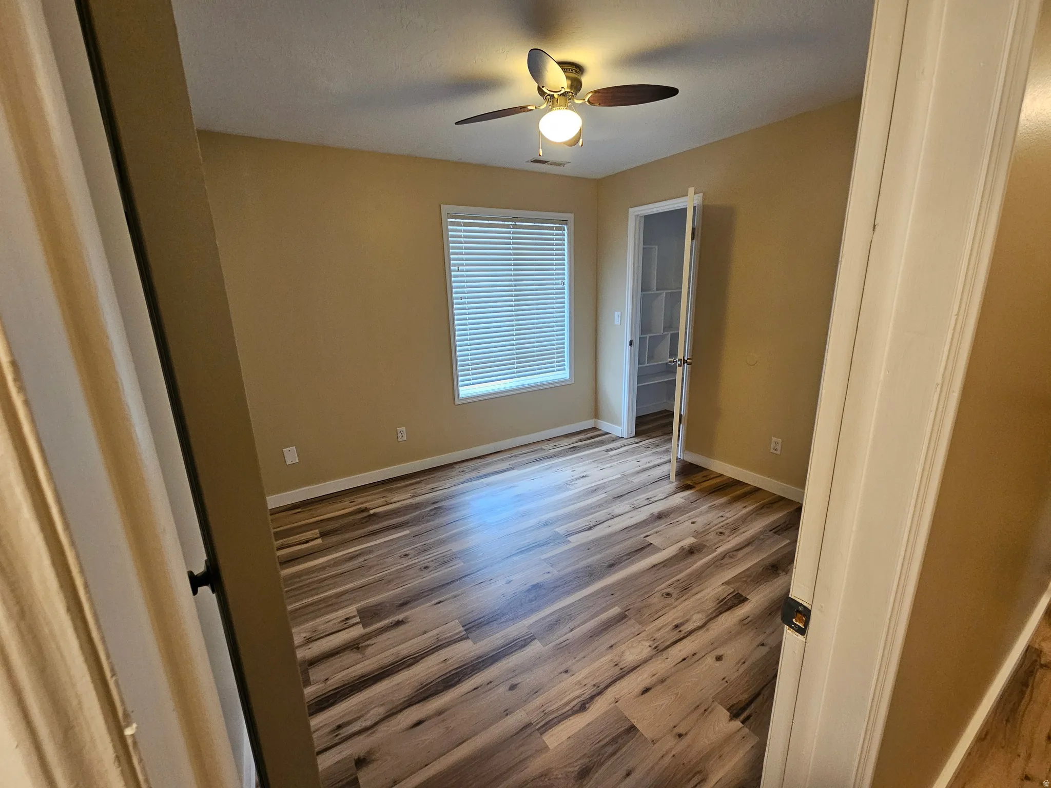 Room featuring wood-finish flooring, a ceiling fan with integrated lighting, and a window with horizontal blinds