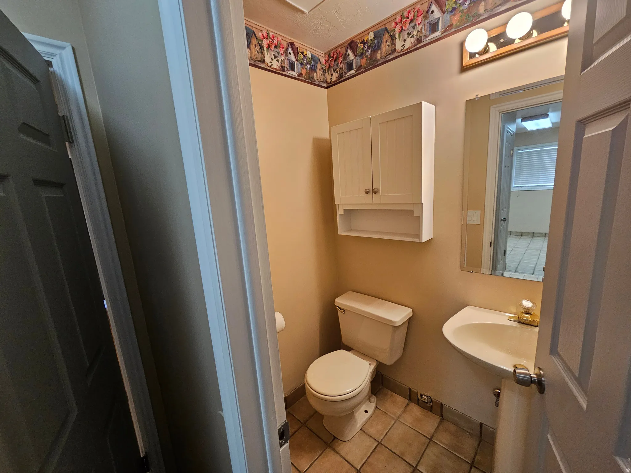 Powder room with a wall-mounted sink, ceramic tile flooring, and a wall-mounted storage cabinet