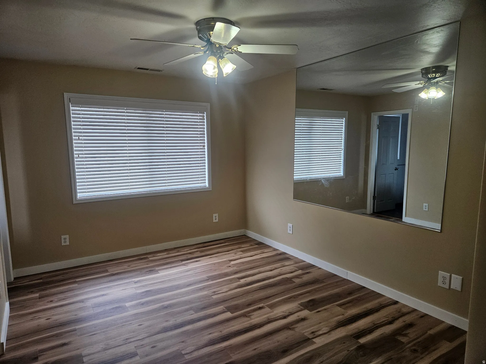 Room featuring wood-finish flooring, a ceiling fan with integrated lighting, and a large wall-mounted mirror