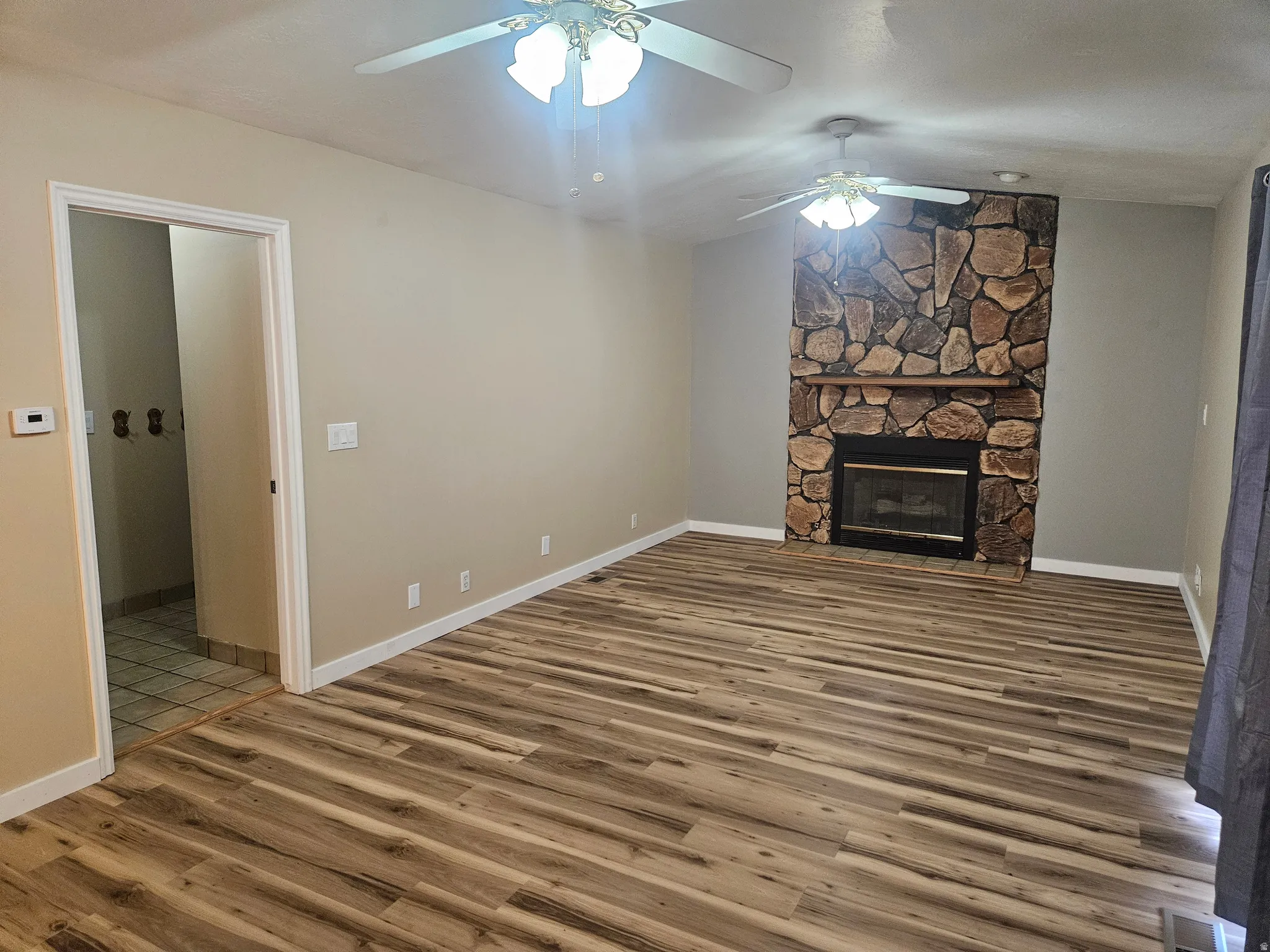 Spacious interior featuring wood-finish flooring, a stone-clad fireplace with a wood mantle, and neutral wall tones