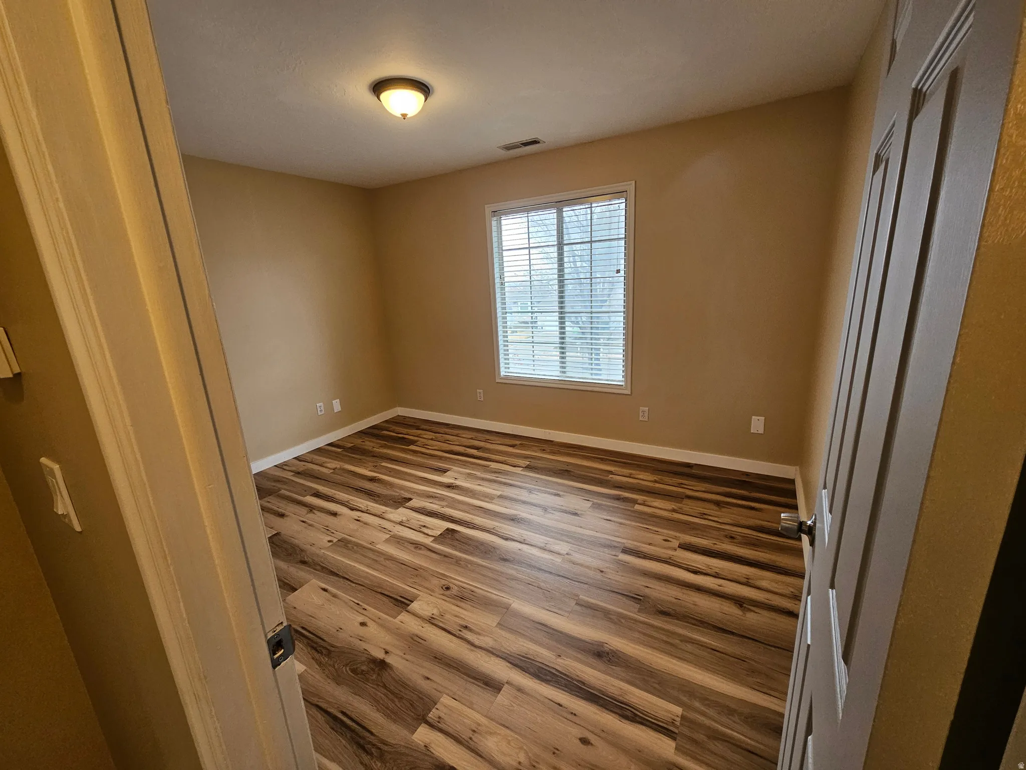 Room featuring wood-finish flooring, neutral wall paint, and a window with horizontal blinds