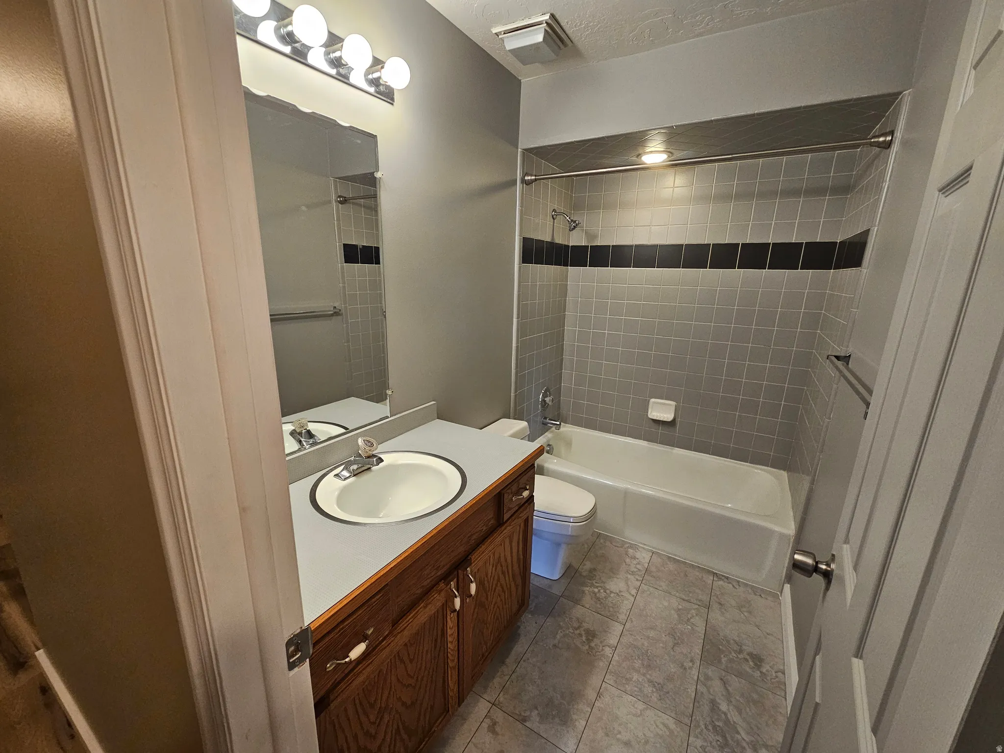 Bathroom featuring a wood-finish vanity with a built-in sink, a large mirror, and a five-bulb light fixture