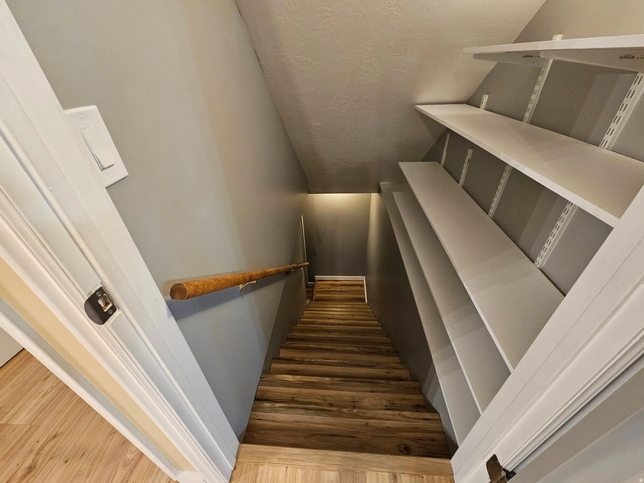 Stairwell featuring wood-finish treads, a wood handrail, and built-in adjustable shelving units