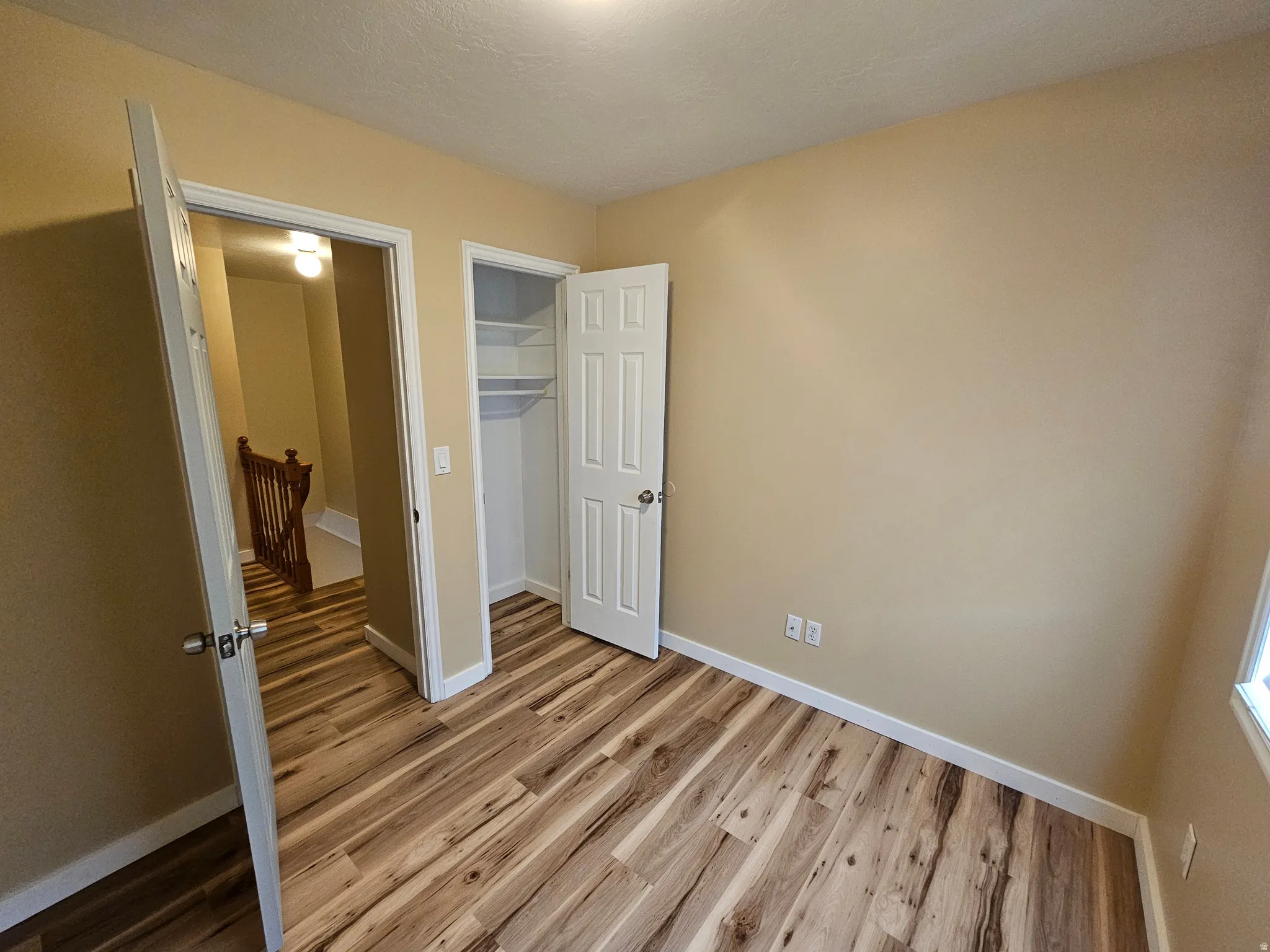 Light-filled room featuring wood-finish flooring, neutral wall tones, white trim, and a built-in closet with shelving