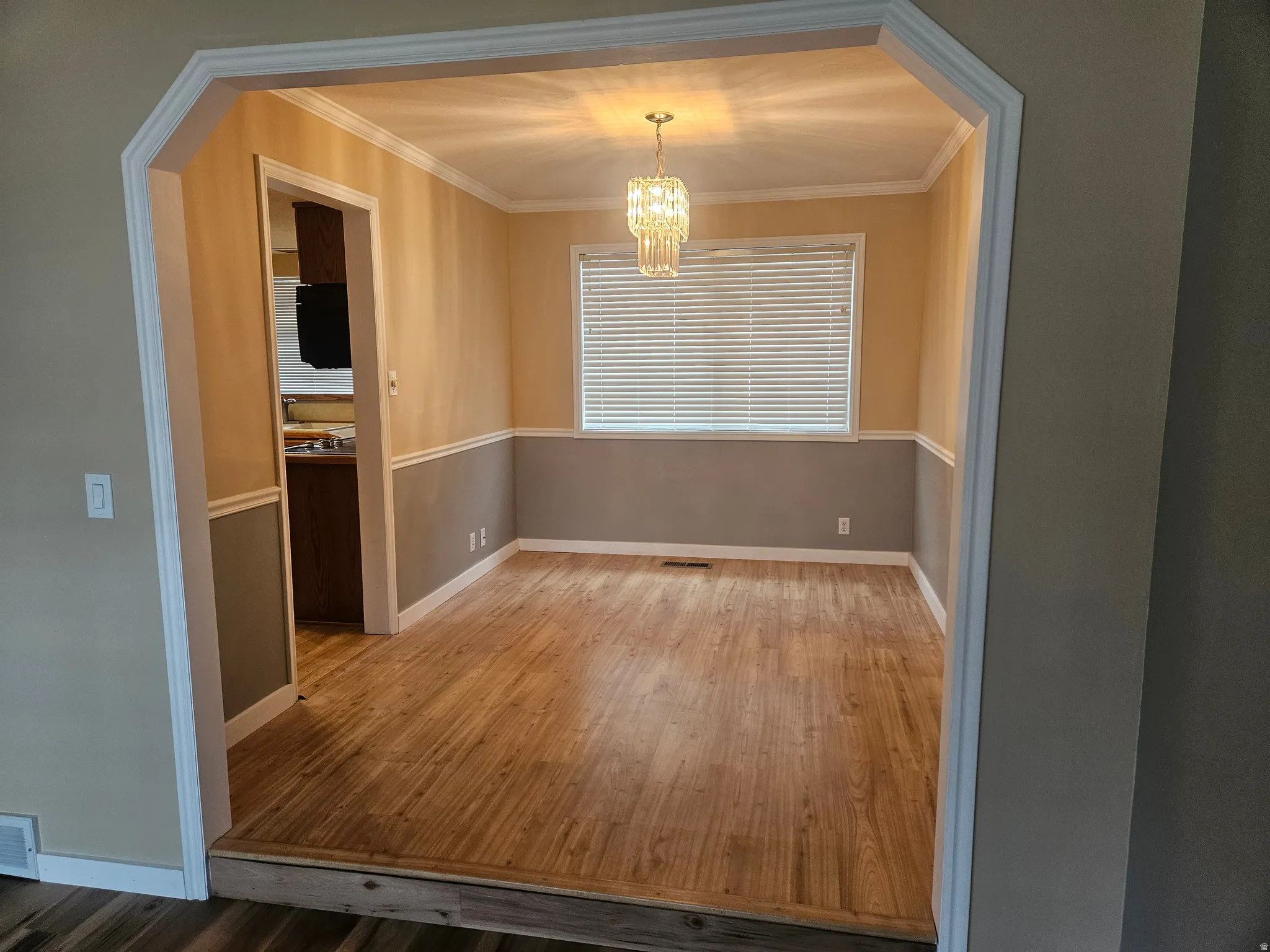Spacious room featuring wood-finish flooring, a contemporary chandelier, crown molding, and two-tone wall treatment