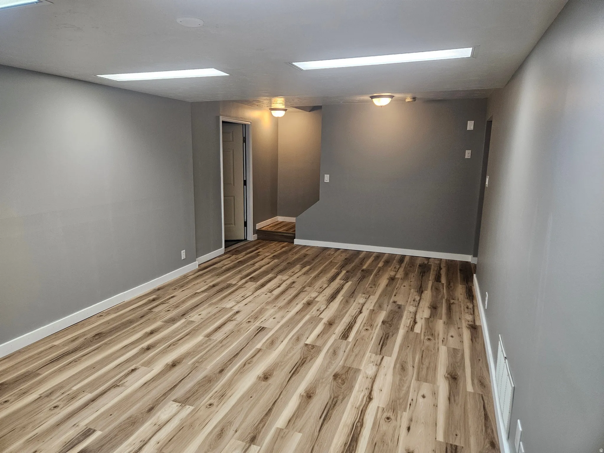 Spacious room featuring wood-finish flooring, white baseboards, and neutral wall tones