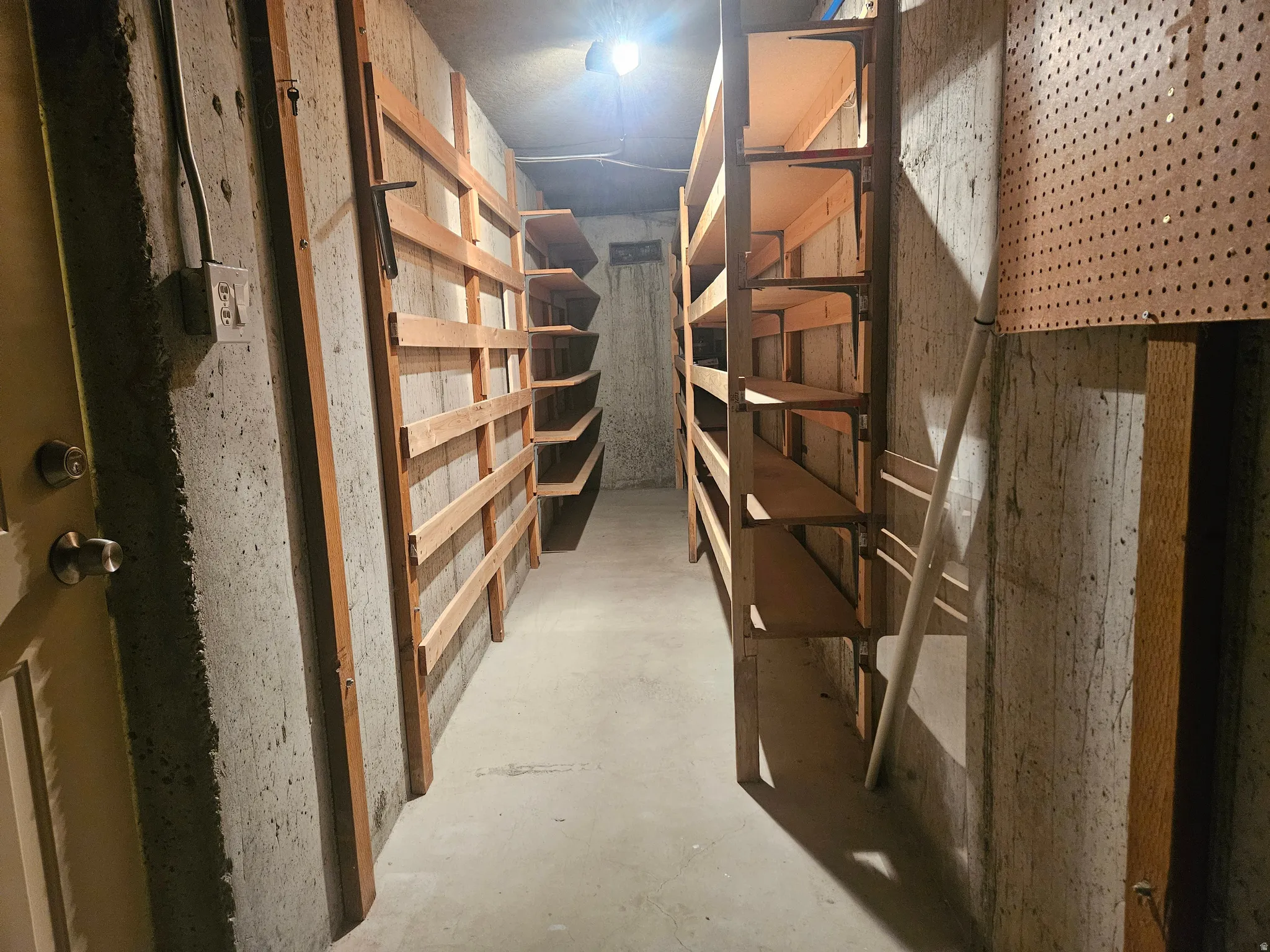 Basement storage area featuring concrete walls, a concrete floor, built-in wood shelving, and a pegboard wall