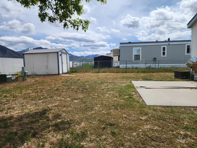 Spacious yard featuring a concrete patio, white storage shed, and chain-link fencing