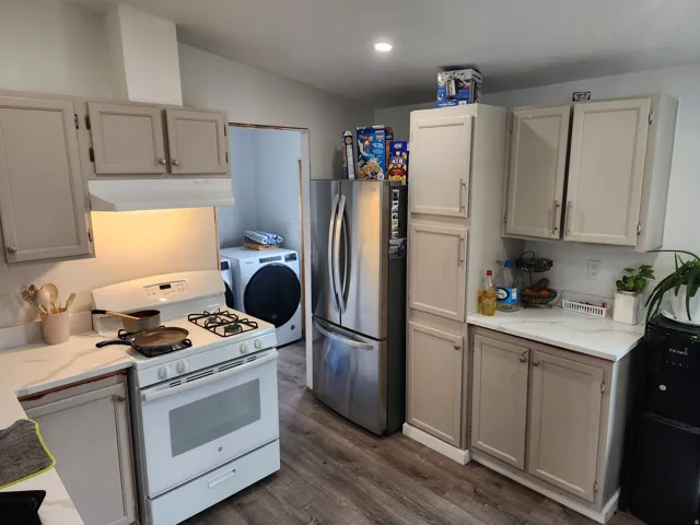 Kitchen featuring white countertops, light taupe cabinetry, wood-finish flooring, a stainless steel refrigerator, and a white gas range with a matching range hood