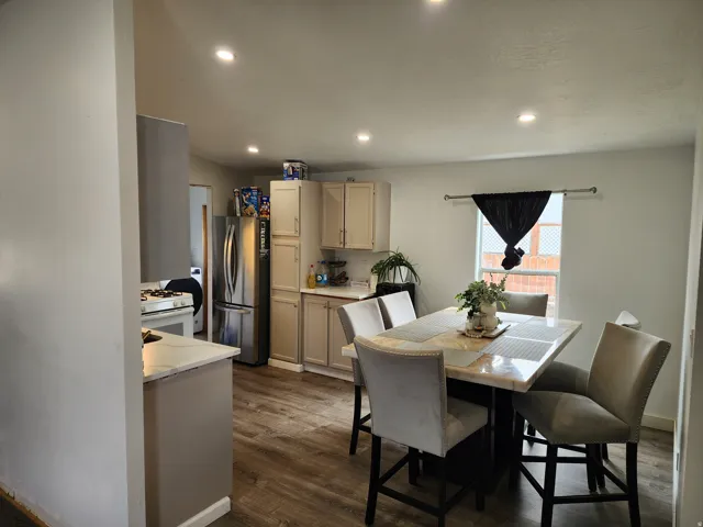 Open-concept kitchen featuring light-toned cabinetry, stainless steel appliances, recessed ceiling lighting, wood-finish flooring, and a dining area with a window
