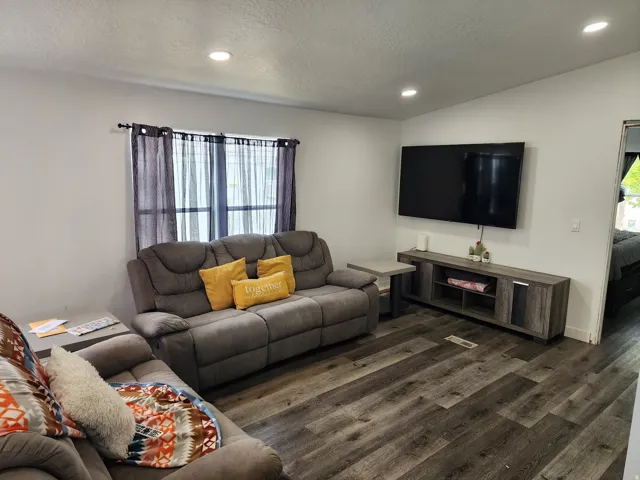 Living area featuring wood-finish flooring, recessed ceiling lighting, a window with vertical blinds, and a built-in media console