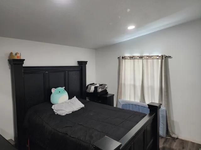 Recessed ceiling lighting illuminates a room with light-colored walls, featuring a window with blinds and curtain rods