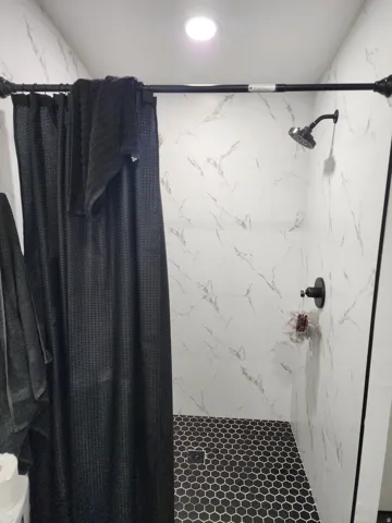 Shower stall featuring white marble-look tile walls and black hexagonal floor tiles