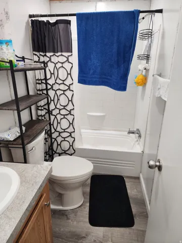 Bathroom featuring a white bathtub, white subway tile surround, wood-finish flooring, and a vanity with a light-toned countertop