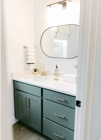Bathroom vanity with a white countertop and integrated sink, featuring a matte green finish on cabinetry and drawers