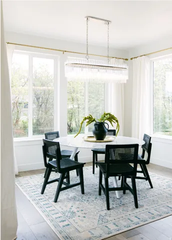 Dining area featuring multiple large windows with white trim, wood-finish flooring, and a linear chandelier with glass rods