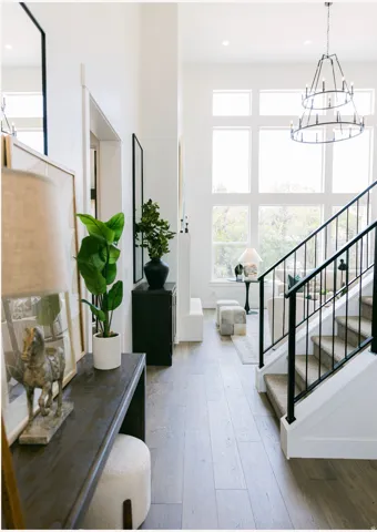 Two-story entry featuring wood-finish flooring, a contemporary chandelier, a white staircase with black iron balusters, and a wall of windows