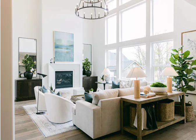 Two-story living area featuring a prominent white fireplace with mantel, double-height windows, a large circular chandelier, and wood-finish flooring