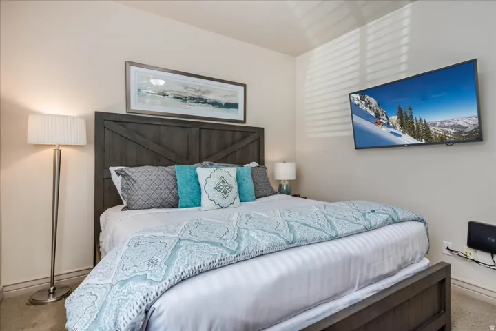 Warm-toned bedroom featuring a dark wood-finish bed frame with a barn-door style headboard, a wall-mounted flat-screen television, and a window with horizontal blinds