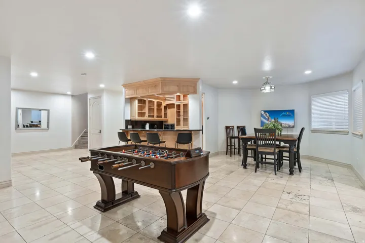 Spacious recreational area featuring light-toned tile flooring, recessed lighting, and a built-in bar with wood cabinetry