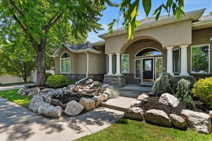 Stucco exterior featuring stacked stone accents, an arched entry, prominent white columns, and a landscaped rock garden