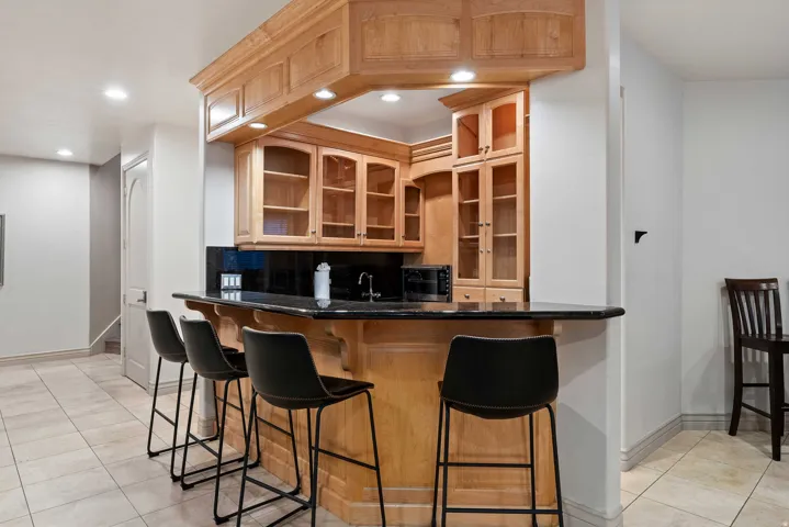 Built-in bar featuring natural wood cabinetry, a dark countertop, an undermount sink, and recessed lighting