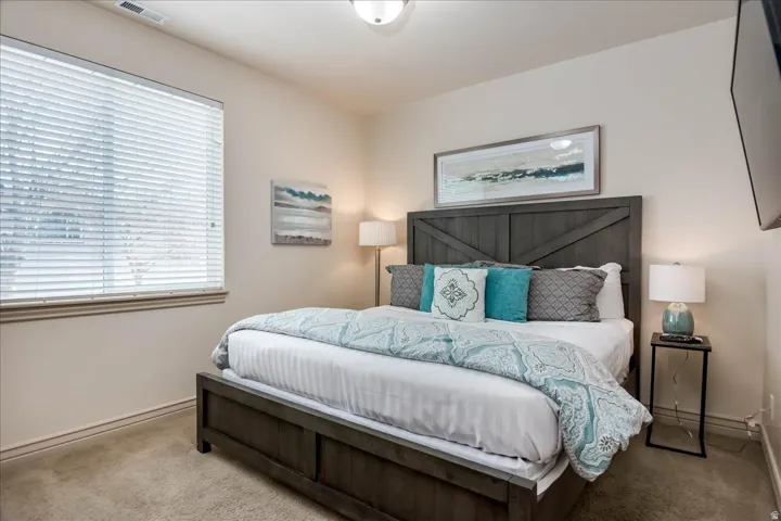 Carpeted bedroom featuring a window with horizontal blinds, neutral wall paint, and a built-in overhead light fixture