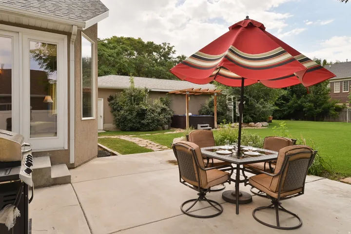 Expansive backyard featuring a large concrete patio, manicured lawn, and mature perimeter trees