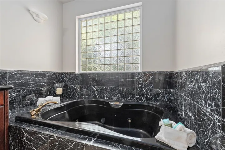 Soaking tub set within a black marble surround, featuring a brass-finish faucet
