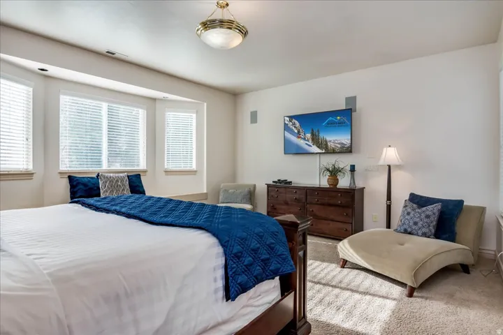 Recessed lighting illuminates a carpeted bedroom with a bay window and blinds