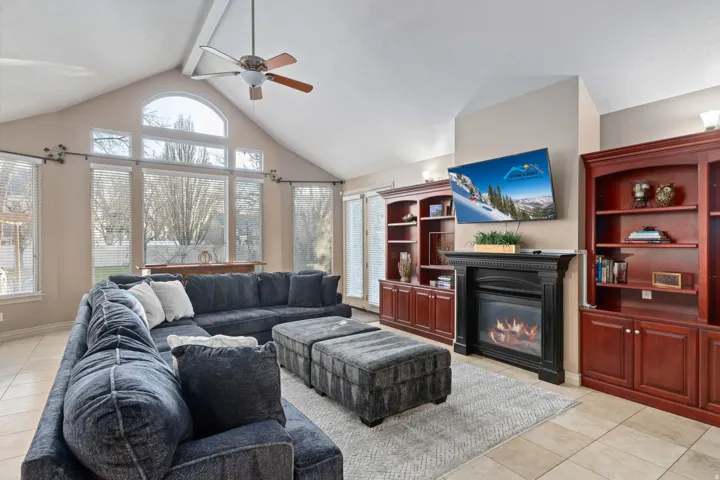Vaulted ceiling living area featuring a gas fireplace, built-in cabinetry, tile flooring, and abundant natural light from multiple windows