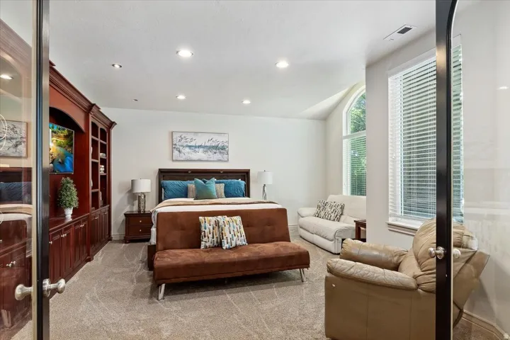Spacious room featuring a large arched window, a built-in media console with shelving and cabinetry, recessed ceiling lighting, and soft carpet flooring