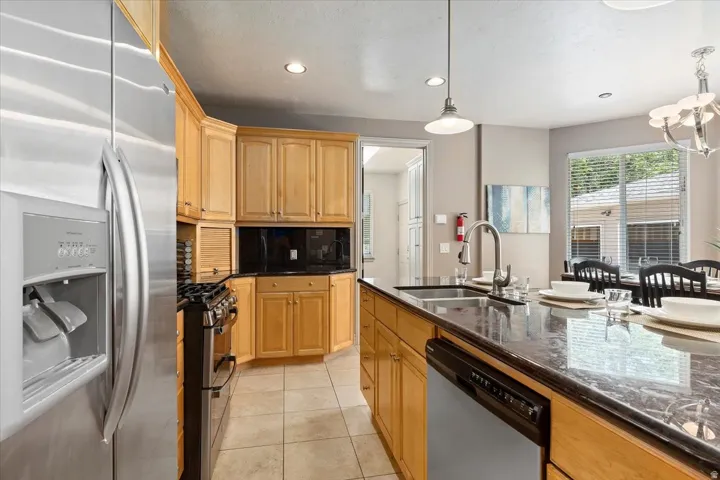Kitchen featuring a stainless steel refrigerator, gas range, wood cabinetry, dark granite countertops, and tile flooring