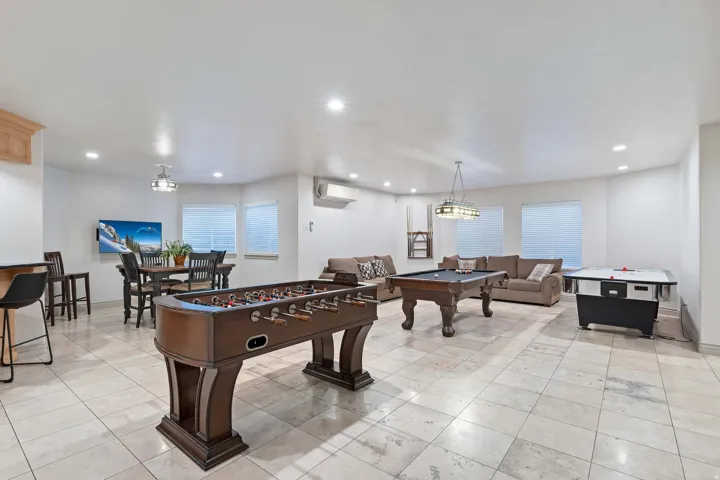 Spacious recreational room featuring light-toned square floor tiles, recessed lighting, and multiple windows