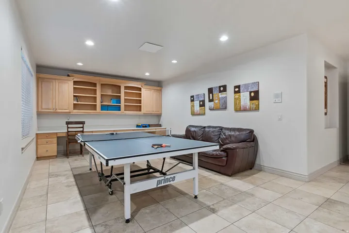 Recessed lighting illuminates a spacious room featuring built-in cabinetry with open shelving, a long integrated desk, and tile flooring