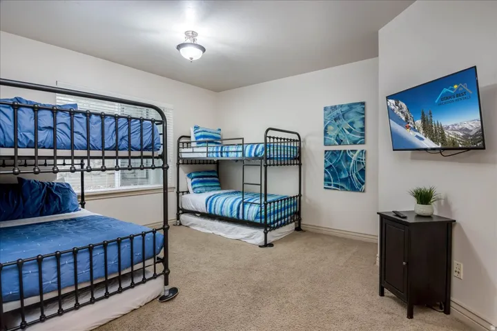Carpeted room featuring bunk beds, a wall-mounted television, and a window with blinds