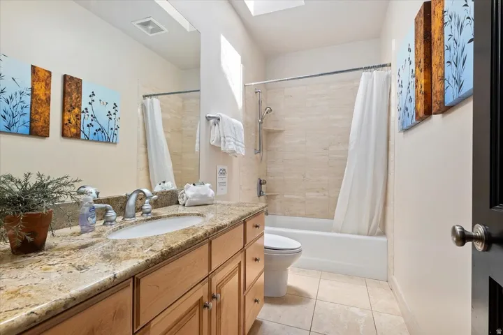 Bathroom featuring a single vanity with a granite countertop, light wood-finish cabinetry, and an undermount sink