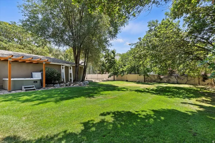 Expansive green lawn surrounded by mature trees, featuring a stucco-sided structure with a wooden pergola and a built-in outdoor spa