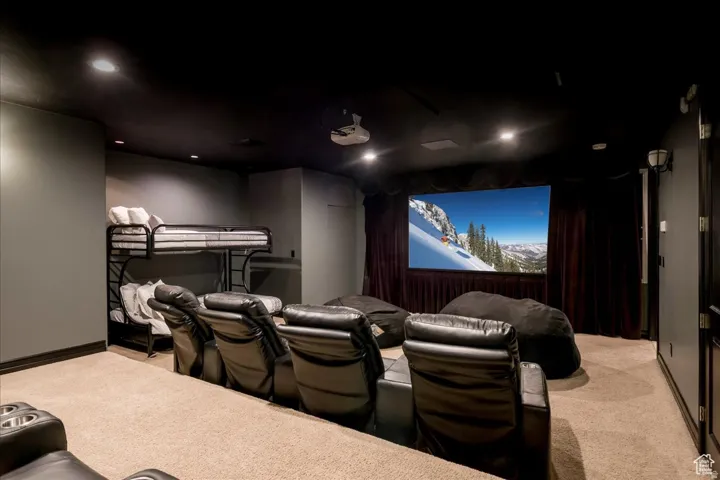 Dedicated media room featuring a large projection screen, recessed lighting, tiered seating in leather recliners, and dark wall coverings
