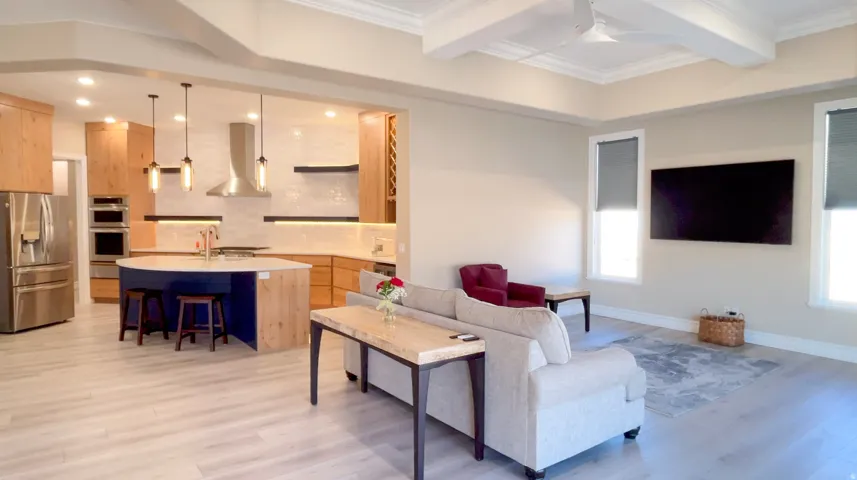 Open-concept living space featuring wood-finish flooring, a tray ceiling with exposed beams, and recessed lighting