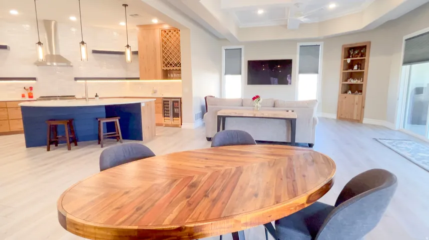 Open-concept living area featuring light wood-finish flooring, a contemporary kitchen with a dark blue island, stainless steel appliances, and a built-in wine rack