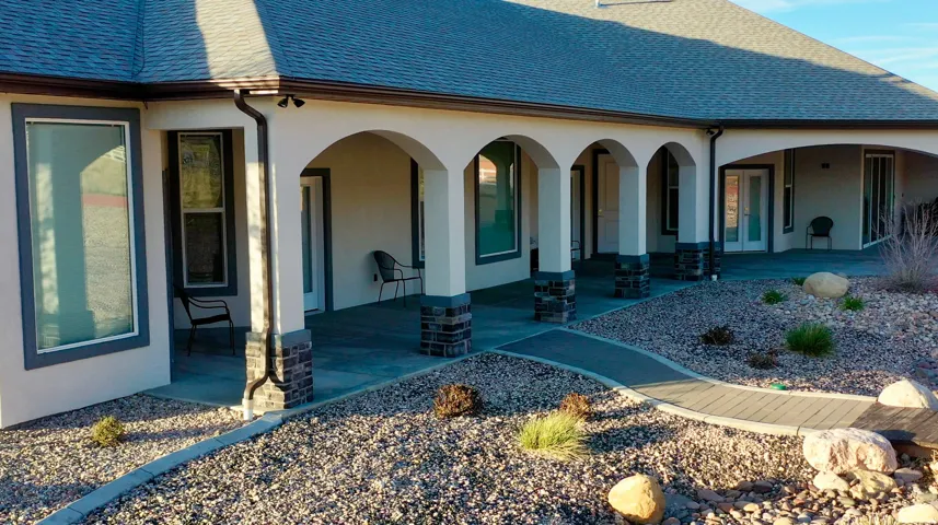 Exterior covered patio featuring arched entries with stone accents, stucco siding, and a low-maintenance landscape