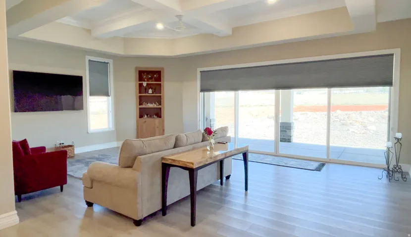 Spacious living area featuring light wood-finish flooring, a coffered ceiling, and expansive sliding glass doors